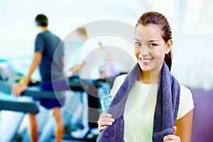 Young woman smiling. Portrait of young smiling woman holding water bottle and towel with people working out in