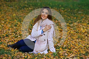 Young woman smiling sitting on the grass in the autum. fall yellow maple garden background