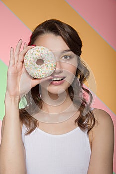 Young woman smiling with a sweet donut in her hands. Portrait on a color background