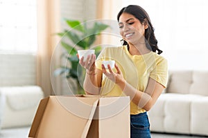 Young Woman Smiling While Unpacking Cardboard Box In Living Room