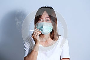 Young woman smoking cigarette with protective mask