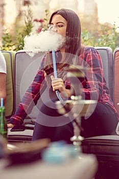 Young woman smoking a hookah outdoors. The pleasure of smoking. City in background