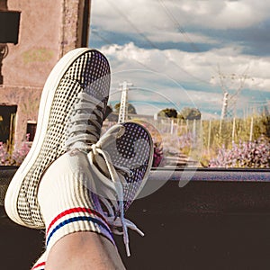 Young woman with sneakers with feet propped on the car window at sunset