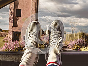 Young woman with sneakers with feet propped on the car window at sunset