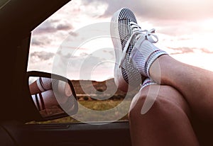 Young woman with sneakers with feet propped on the car window at sunset