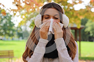 Young woman sneezing and blowing nose into tissue outdoors
