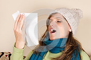 Young woman sneezing in a tissue in the living room,