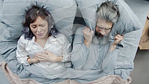 Young woman snoring in sleep while irritated husband covering head with pillow