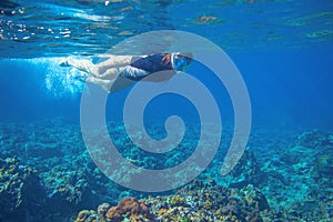 Young woman snorkeling underwater photo. Snorkel in coral reef of tropical sea. Young girl in fullface snorkeling mask