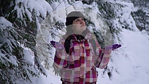 Young woman in the snowy woods. Young pretty tourist stands alone in the forest and looks around. She catches snowflakes