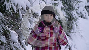 Young woman in the snowy woods. Young pretty tourist stands alone in the forest and looks into the camera. She is calm