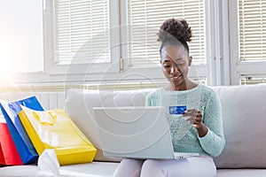 Young Woman On Sofa Shopping Online With Laptop. Young black woman inputting card information while shopping online. Online