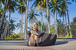 Young woman on a soft board for a trampoline jumping on an outdoor trampoline, against the backdrop of palm trees. The