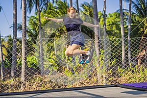 Young woman on a soft board for a trampoline jumping on an outdoor trampoline, against the backdrop of palm trees. The