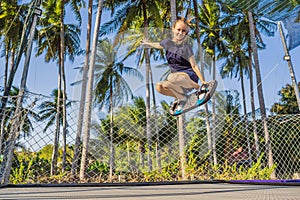Young woman on a soft board for a trampoline jumping on an outdoor trampoline, against the backdrop of palm trees. The