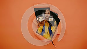 Young woman with soft puppet toys on hands looking out of hole of orange background. Pretty female with puppet monkey