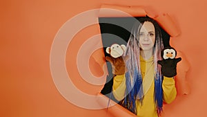 Young woman with soft puppet toys on hands looking out of hole of orange background. Pretty female with puppet monkey