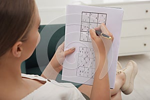 Young woman solving sudoku puzzle on sofa, closeup