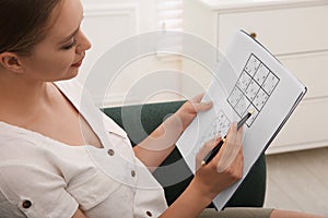 Young woman solving sudoku puzzle on sofa indoors, closeup