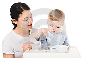 young woman with son in bib eating and sitting highchair