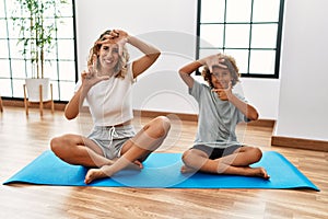 Young woman and son sitting on training mat at the gym smiling making frame with hands and fingers with happy face