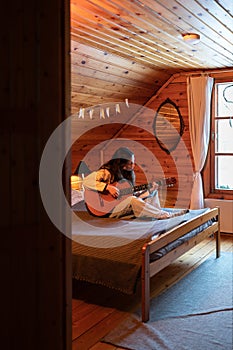 Young woman songwriter or composer sitting in cozy attic bedroom playing guitar, creating melody