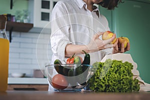 Young Woman sorting green fresh vegetables from shopping bag while standing in kitchen at home