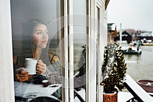 Young woman spending free time home.Self care,staying home.Enjoying view,gazing through to the window.Quarantined person indoors.