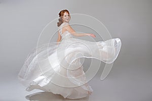 Young woman spinning in a curvy wedding dress. woman bride in lavish wedding dress. Light background.