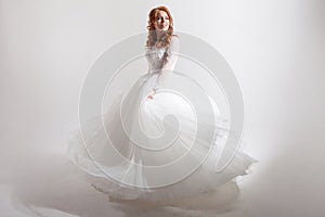 Young woman spinning in a curvy wedding dress. woman bride in lavish wedding dress. Light background.