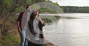 Young woman with spinning and her boyfriend on the lake are fishing.