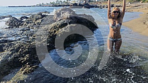 Young woman splashes water in camera standing at seashore