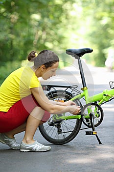 Young woman in sport clothes repairs bike in park