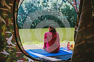 Young woman in the sport wear outfit is sitting and relaxing in the camping in the forest