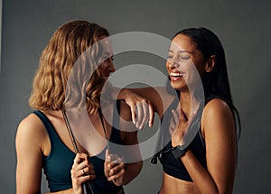 Young woman in sports bra holding jump rope while laughing with friend