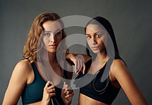 Young woman in sports bra holding jump rope while looking at camera with friend