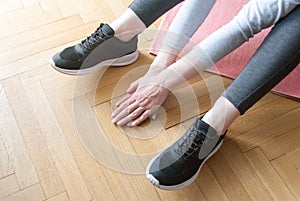 Young woman in sports wear doing stretching at loft studio on sport mat. Legs and hands close up. Workout and healthy life concept