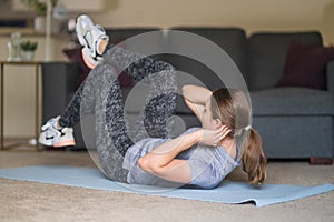 Young woman in sports wear pumps the press on the fit mat in living room at home. Healthy lifestyle concept. Stay at home