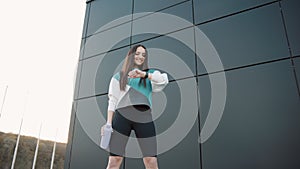 Young woman in sportswear with a bottle look at smart watch while jogging at city public park