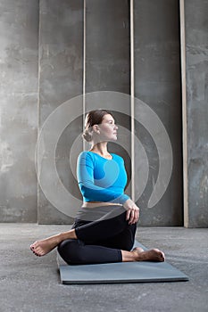 A young woman in sportswear does a back twist while sitting on a yoga mat. Pilates, a healthy back class.