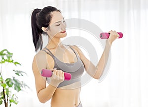 Young woman in sportswear doing fitness stretching exercises with dumbbell at home