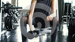 Young woman in sportswear doing seated dumbbell concentration curl bicep exercise at the gym.