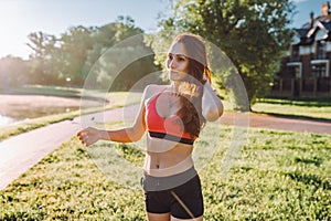 Young woman in sportswear doing workout in green park near house in sunny day.