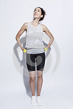 Young woman in sportswear with dumbbells. Smiling brunette. Full height. White background, hard light. Vertical