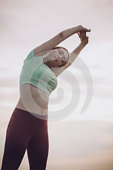 Young woman in sportswear exercises and stretches hands up, girl engaged in sport outdoors view from below, concept health and