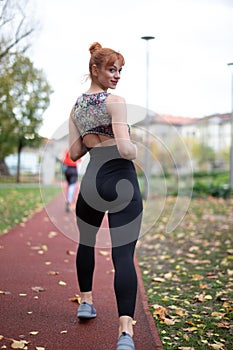 Young woman in sportswear looking back while quick walking at autumn