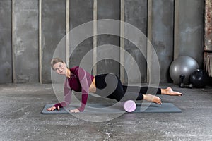 A young woman in sportswear performs a myofascial massage of the lower leg muscles with a roller. Muscle recovery, mfr.