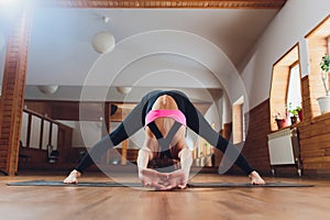 Young woman in sportswear practicing yoga, standing in prasarita padottanasana.