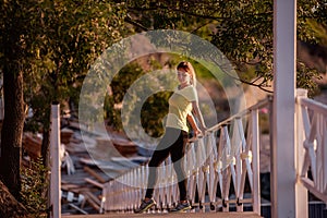 Young woman in sportswear is resting after workout, walking along wooden stairs in the rays of sun