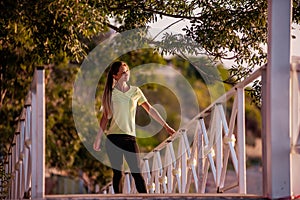 Young woman in sportswear is resting after workout, walking along wooden stairs in the rays of sun